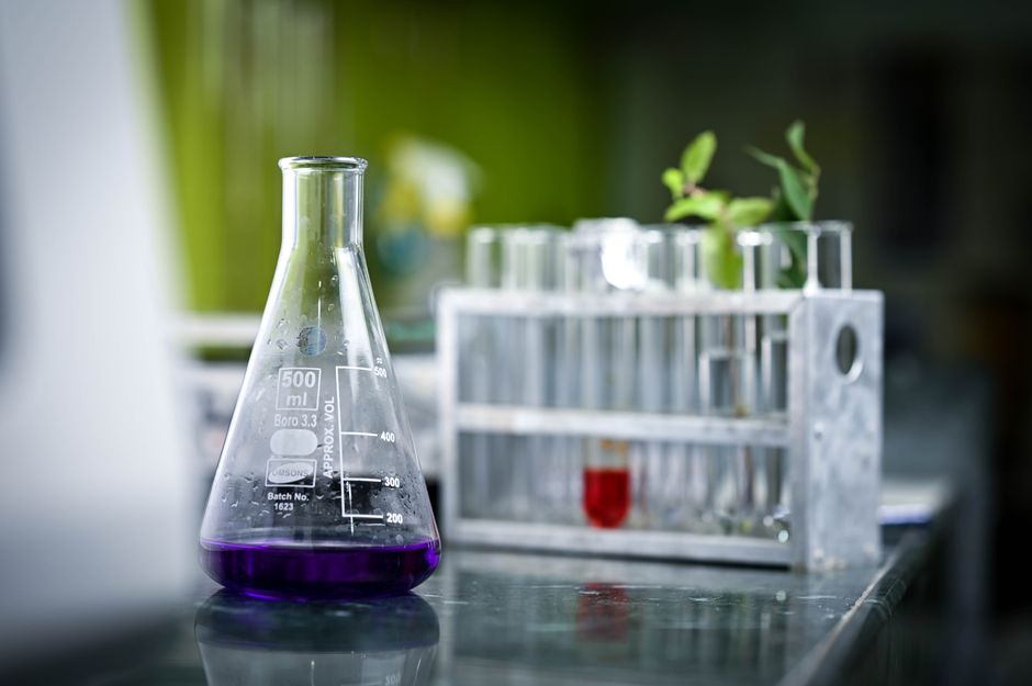 Close-up of a lab flask with purple liquid and test tubes in a scientific setting.
